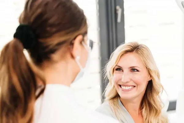 Blick über die Schulter einer Zahnärztin auf eine lächelnde Patientin